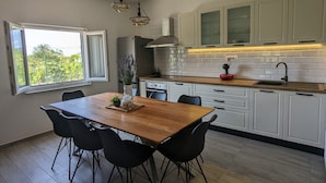 A modern kitchen with white cabinets, a wooden dining table, black chairs, and pendant lights. - Runaway Cottage Villa (Unesic)