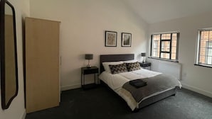 Un dormitorio con una cama, dos mesitas de noche, un espejo y una ventana.