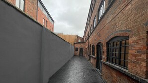 Un estrecho callejón flanqueado por edificios de ladrillo, uno con un amplio ventanal y otro con fachada plana.