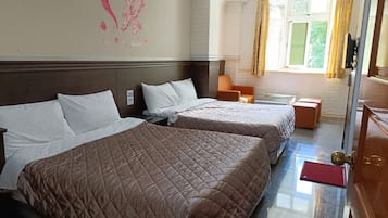 A hotel room with two beds, a wooden headboard, a small table, and a window with curtains.