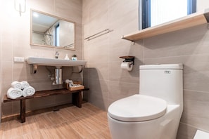 Un baño moderno con inodoro blanco, lavamanos con espejo y banco de madera.