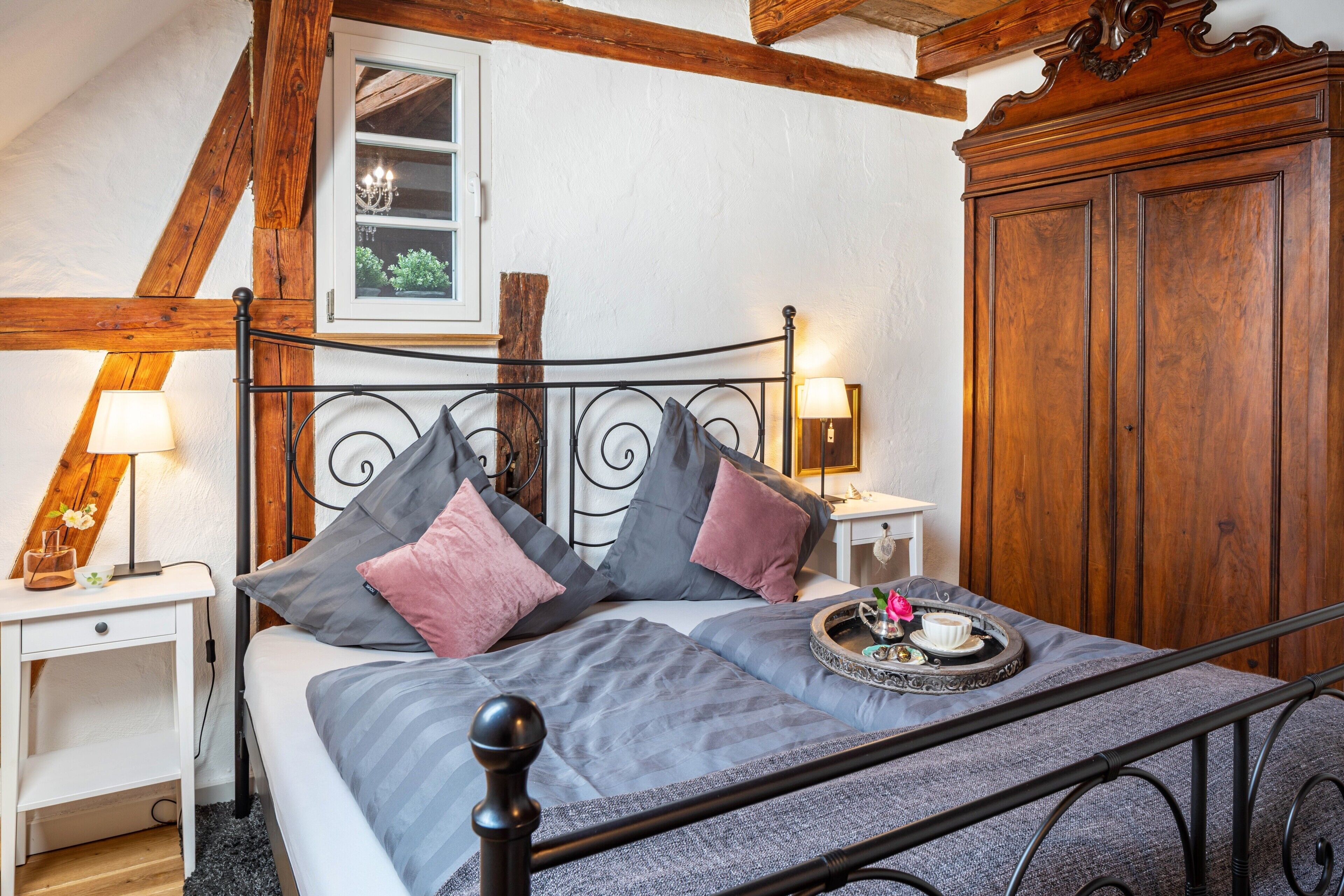 A bedroom with a bed, bedside tables, a nightstand, a wooden wardrobe, and a window with a view.