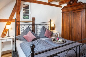 A bedroom with a bed, bedside tables, a nightstand, a wooden wardrobe, and a window with a view.