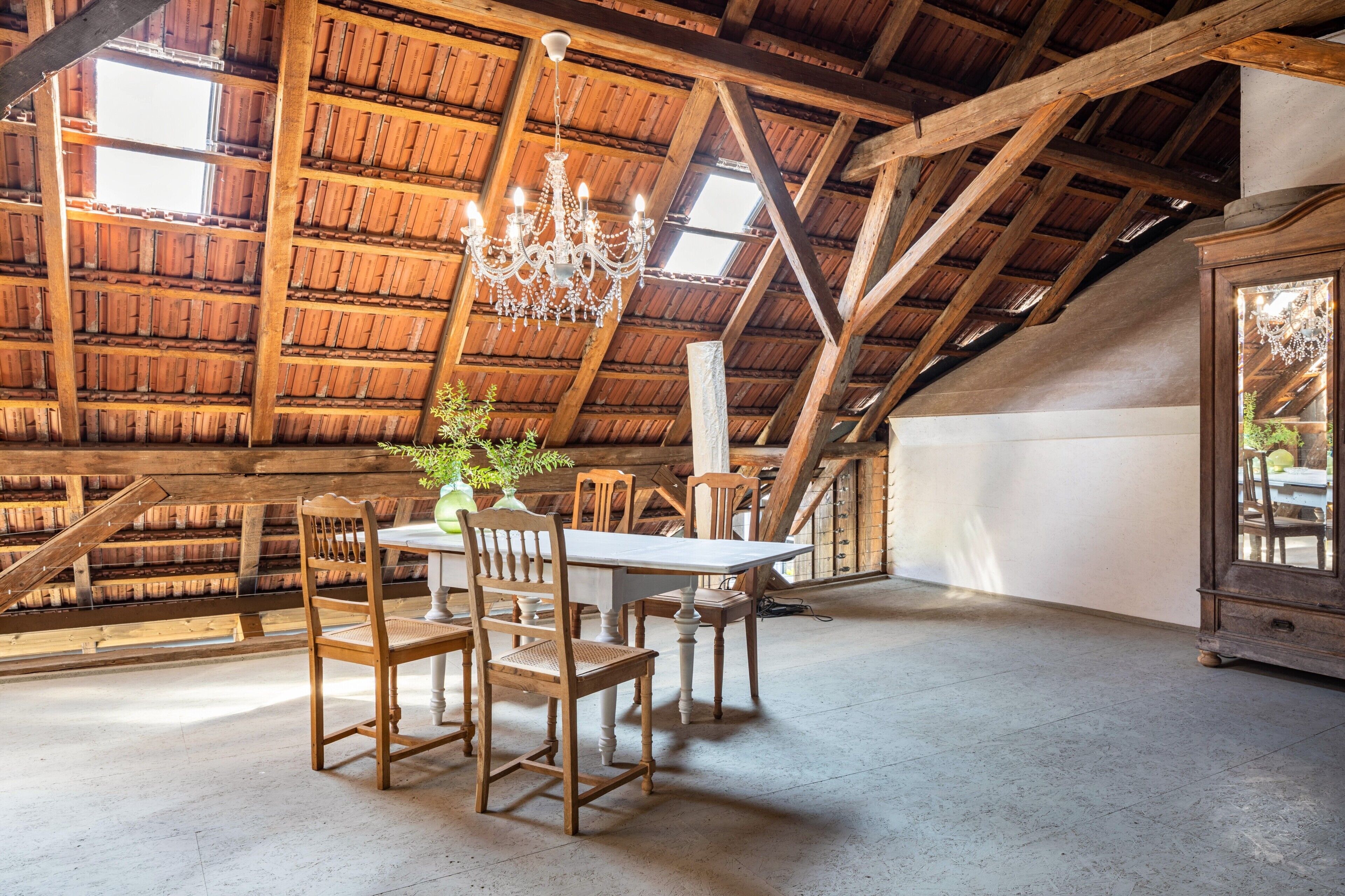 A dining area with wooden chairs and a table, a chandelier, and a large window.