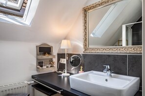A modern bathroom with a skylight, a large mirror, a sink, and a vanity with a lamp.