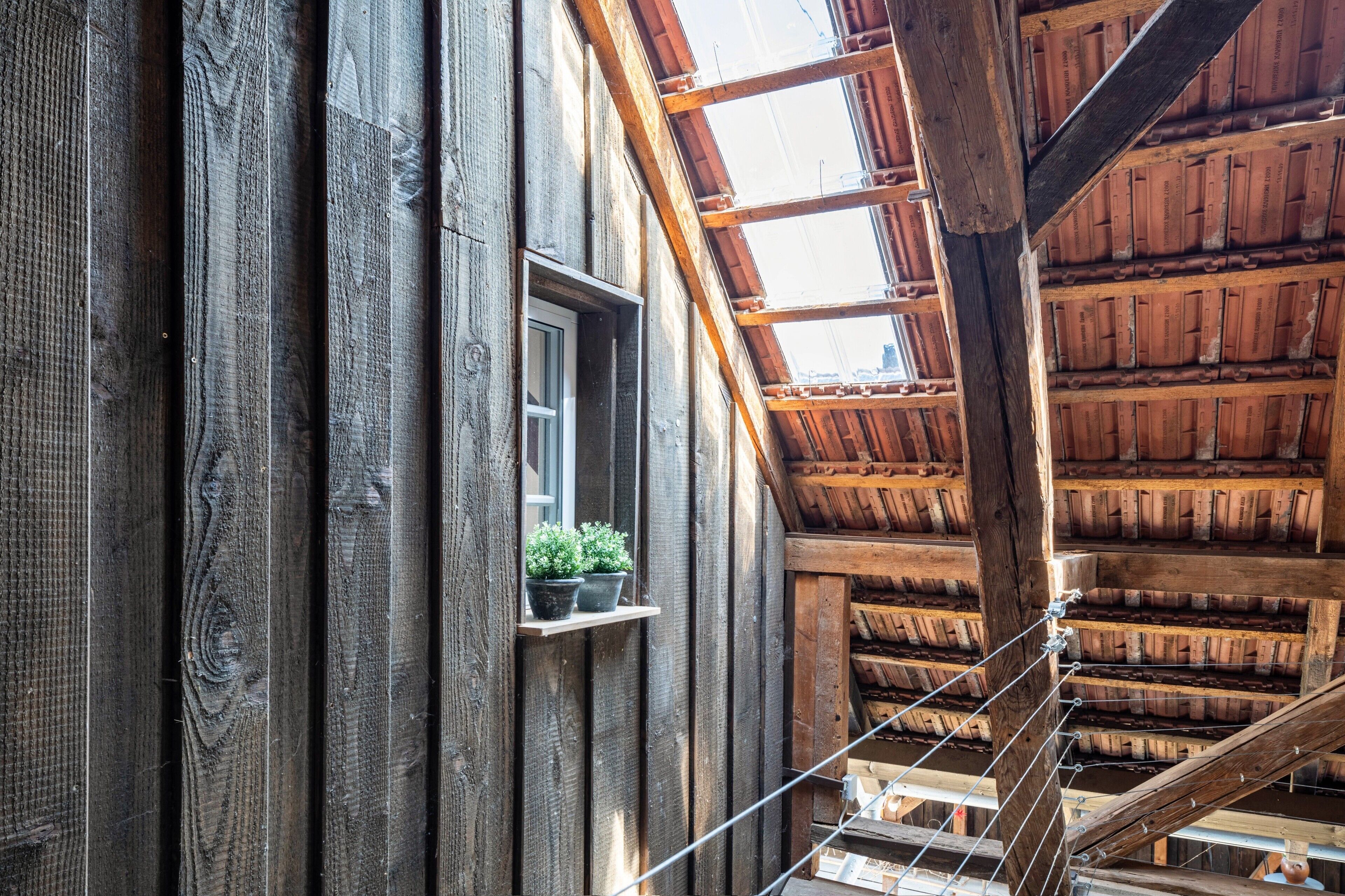 Ein Holzinnenraum mit Fenster, Holzbalken und schrägverlaufender Decke.