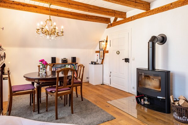 A cozy room with a dining table, chairs, a chandelier, a fireplace, and wooden beams on the ceiling.