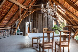 An attic room with a wooden ceiling, a chandelier, a dining table, and wooden chairs.
