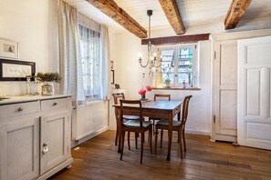A dining area with a wooden table and chairs, a white cabinet, and a window with curtains.