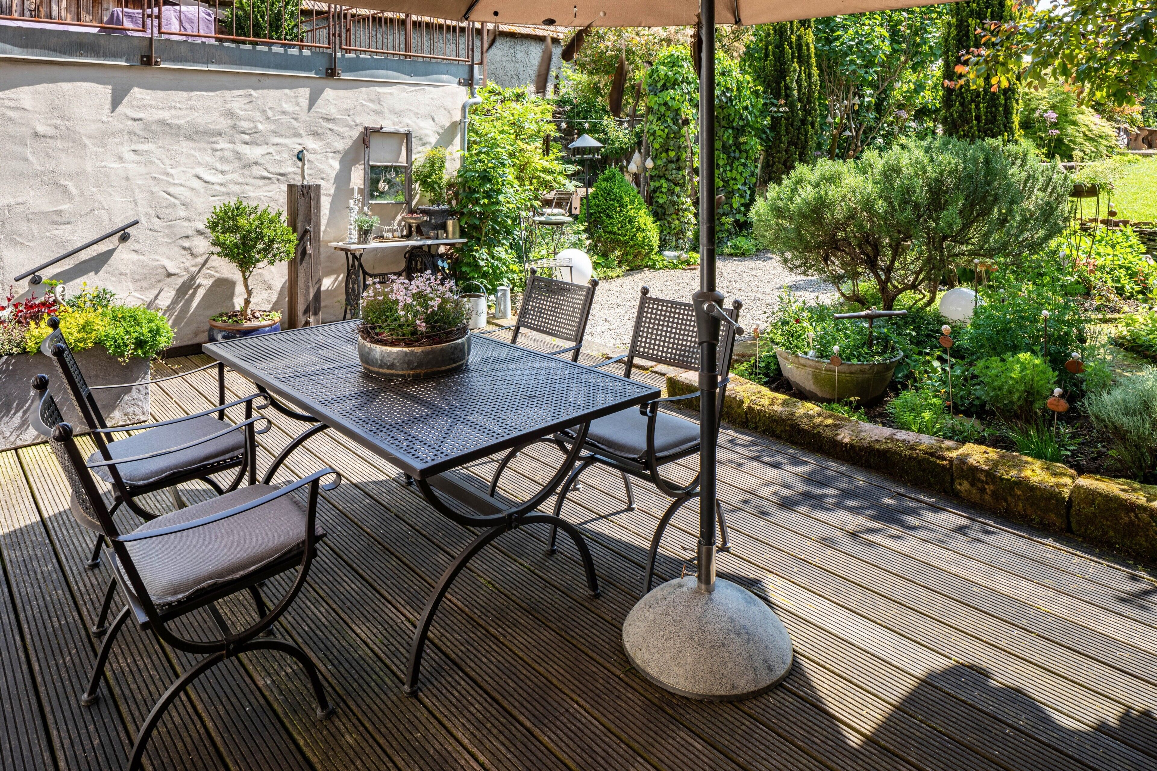 Eine Terrasse im Freien mit Tisch und Stühlen, umgeben von Kübelpflanzen und einem Garten.