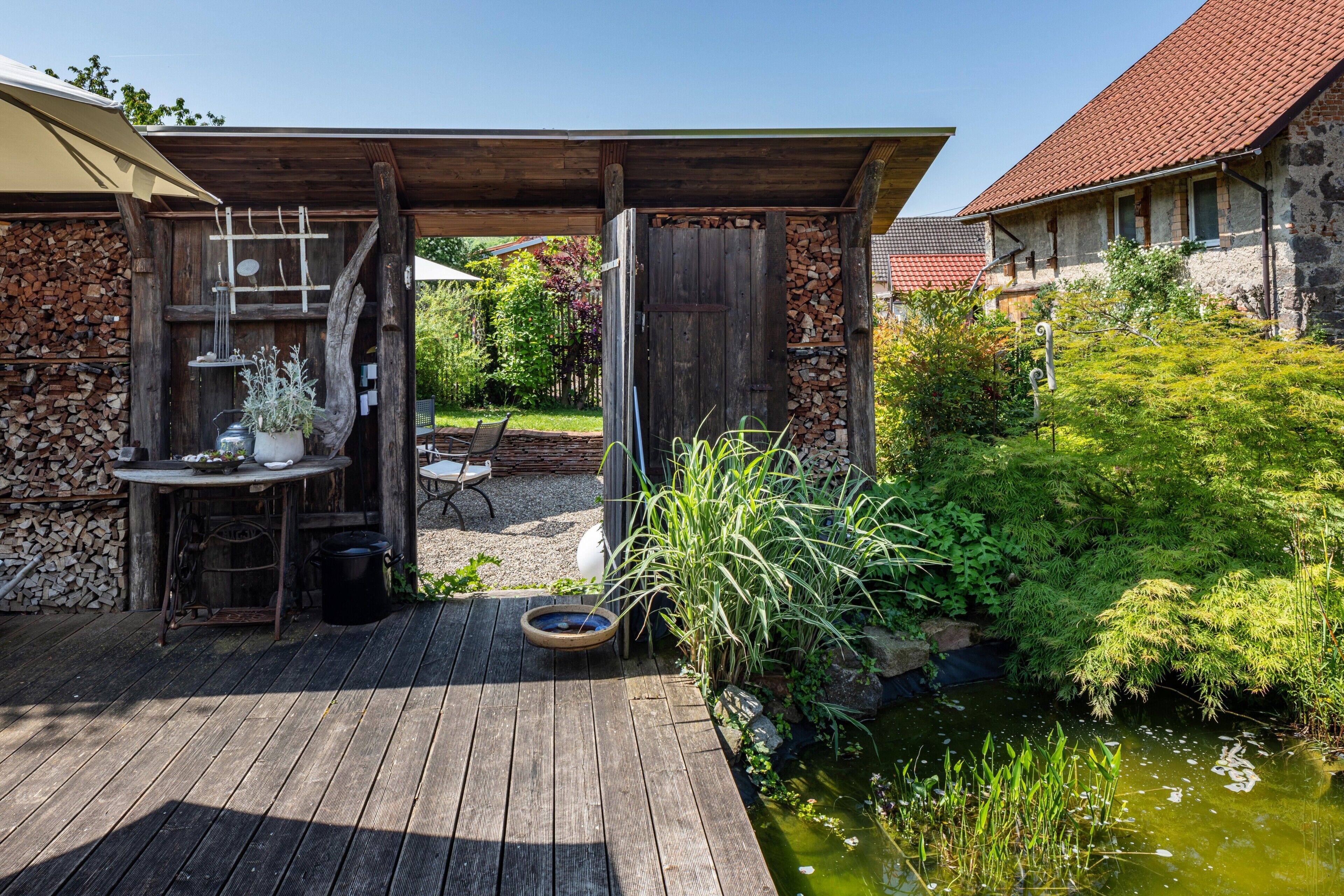 A wooden deck with a table and chairs, a small pond, and a stone wall.