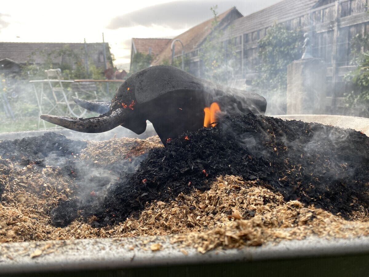A large black elephant statue with a long trunk, surrounded by a pile of dark, ash-like material, possibly charcoal, with some red objects scattered around.