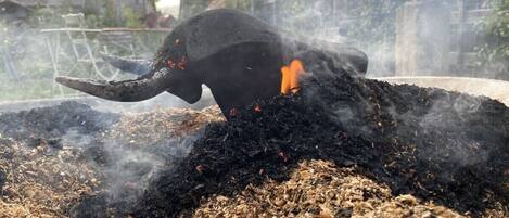 A large black elephant statue with a long trunk, surrounded by a pile of dark, ash-like material, possibly charcoal, with some red objects scattered around.