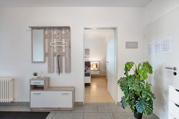 A modern hotel room with a wooden vanity, a mirror, a radiator, a potted plant, and a view into the adjacent bedroom.