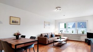 A modern living room with a wooden dining table, a brown sofa, and a TV.