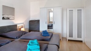 A hotel room with two beds, a wardrobe, a mirror, and a painting on the wall.