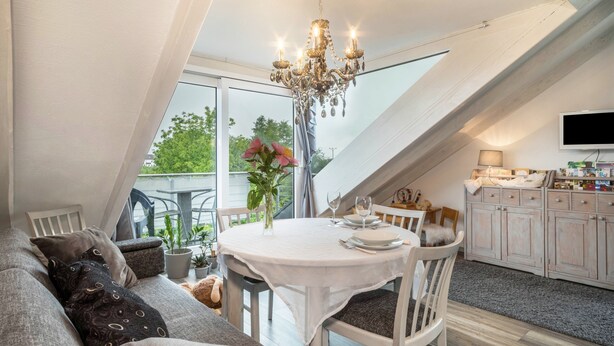 Ein Essbereich mit Tisch für zwei Personen, einer Chandelüster und Blick durch eine Dachfenster.