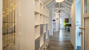 Ein Flur mit weißen Regaleinheiten, Holzdielenboden und einer Decke mit freiliegenden Balken und Pendelleuchten.