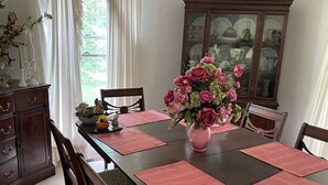 Une salle à manger avec une table en bois, des sets de table roses et un vase rempli de fleurs roses.