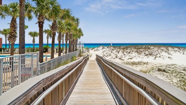 A wooden boardwalk leading to a beach with palm trees and a clear blue sky. - Renovated Condo: 3 Min Beach Walk (Destin)