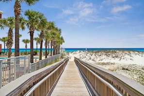 A wooden boardwalk leading to a beach with palm trees and a clear blue sky.
