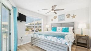A bedroom with a bed, a ceiling fan, a TV mounted on the wall, and a window with blinds. - Renovated Condo: 3 Min Beach Walk (Destin)