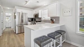 A modern kitchen with white cabinetry, stainless steel appliances, and a central island with bar stools. - Renovated Condo: 3 Min Beach Walk (Destin)