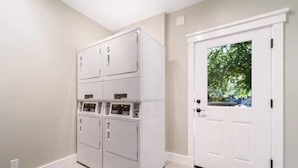 A laundry room with four stacked washers and dryers, a white door with a window, and beige walls. - Comfortable Modern Condo near Downtown (Friday Harbor)