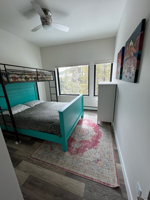 A bedroom with a bunk bed, a ceiling fan, large windows, a radiator, and a rug.