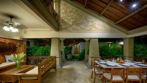 A spacious indoor dining area with wooden furniture, a central staircase, and a view of a lush garden. - villa deh simba at seminyak oberoi  (Seminyak)