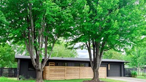 Una casa moderna con garaje, rodeada de un césped cuidado y dos árboles grandes.