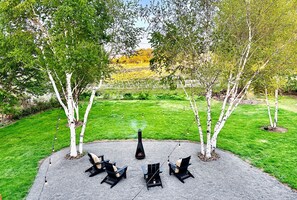 A circular outdoor seating area with three black chairs and a table, surrounded by a gravel path. - Mid Century Modern - Heart of Wine Country (Milton-Freewater)