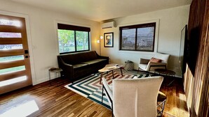 Una sala de estar moderna con piso de madera, un sofá marrón, un sillón blanco y una alfombra estampada.