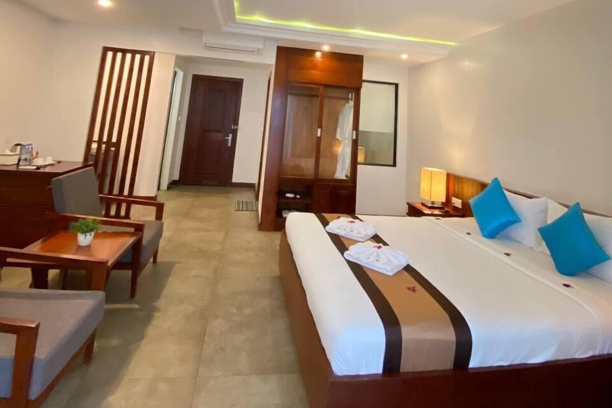 A hotel room with a large bed, a desk, a chair, and a wardrobe.