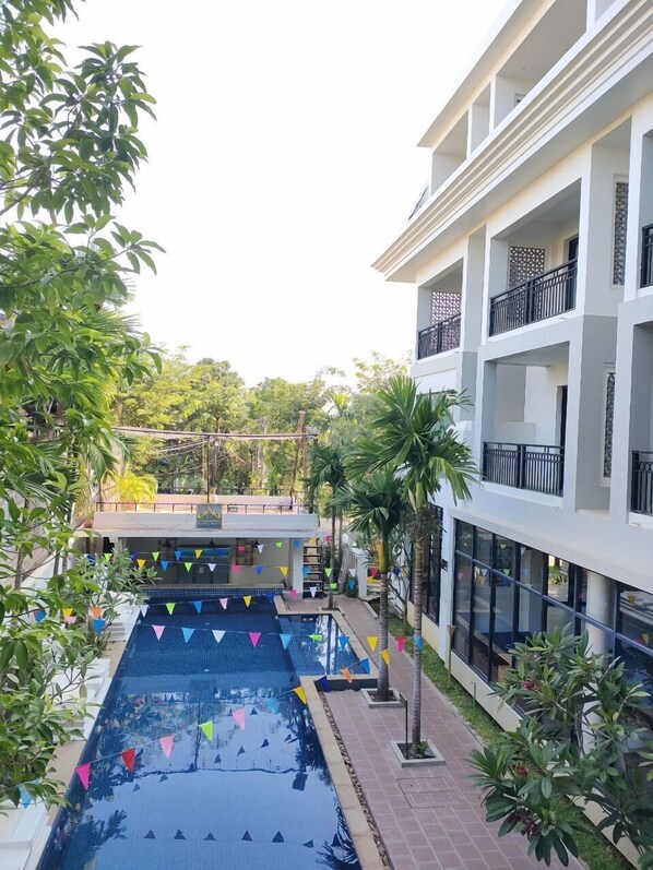 A swimming pool with colorful flags, surrounded by a multi-story building with balconies and a garden area.