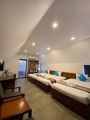 A hotel room with three beds, a dining area, and a small kitchenette.