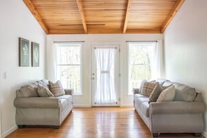 Habitació amb dos sofàs, sostre de fusta i una porta amb cortines.