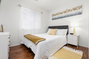 A bedroom with a bed, nightstand, lamp, and a painting on the wall. - Bright & Comfy House Near NAS with Free Parking (Armona)