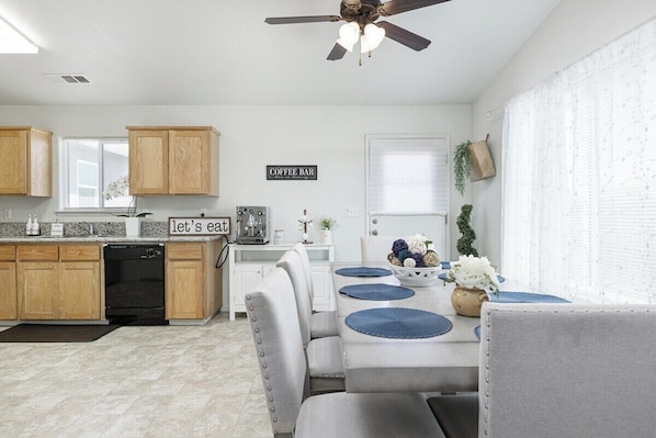 A modern kitchen with wooden cabinets, a coffee bar sign, and a dining area with a table and chairs. - Bright & Comfy House Near NAS with Free Parking (Armona)
