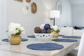 Un área de comedor con una mesa dispuesta, con manteles individuales, un cuenco de adornos y un florero con flores.