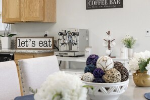 A kitchen with a coffee machine, a sign that says 'let's eat,' and a bowl of decorative balls on the counter. - Bright & Comfy House Near NAS with Free Parking (Armona)