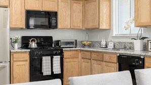 A kitchen with wooden cabinets, a microwave, a stove, a dishwasher, and a window with blinds. - Bright & Comfy House Near NAS with Free Parking (Armona)