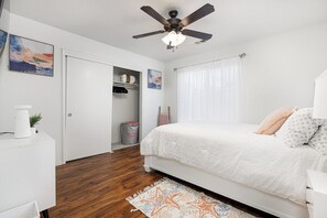 A bedroom with a bed, a ceiling fan, a white wardrobe, a small table, and a window with curtains. - Bright & Comfy House Near NAS with Free Parking (Armona)