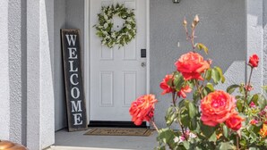 A white door with a wreath, a 'WELCOME' sign, and red roses in the foreground. - Bright & Comfy House Near NAS with Free Parking (Armona)