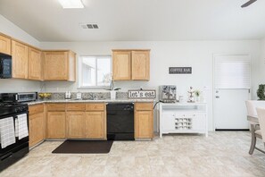 A modern kitchen with wooden cabinets, a dishwasher, a microwave, and a coffee bar sign. - Bright & Comfy House Near NAS with Free Parking (Armona)