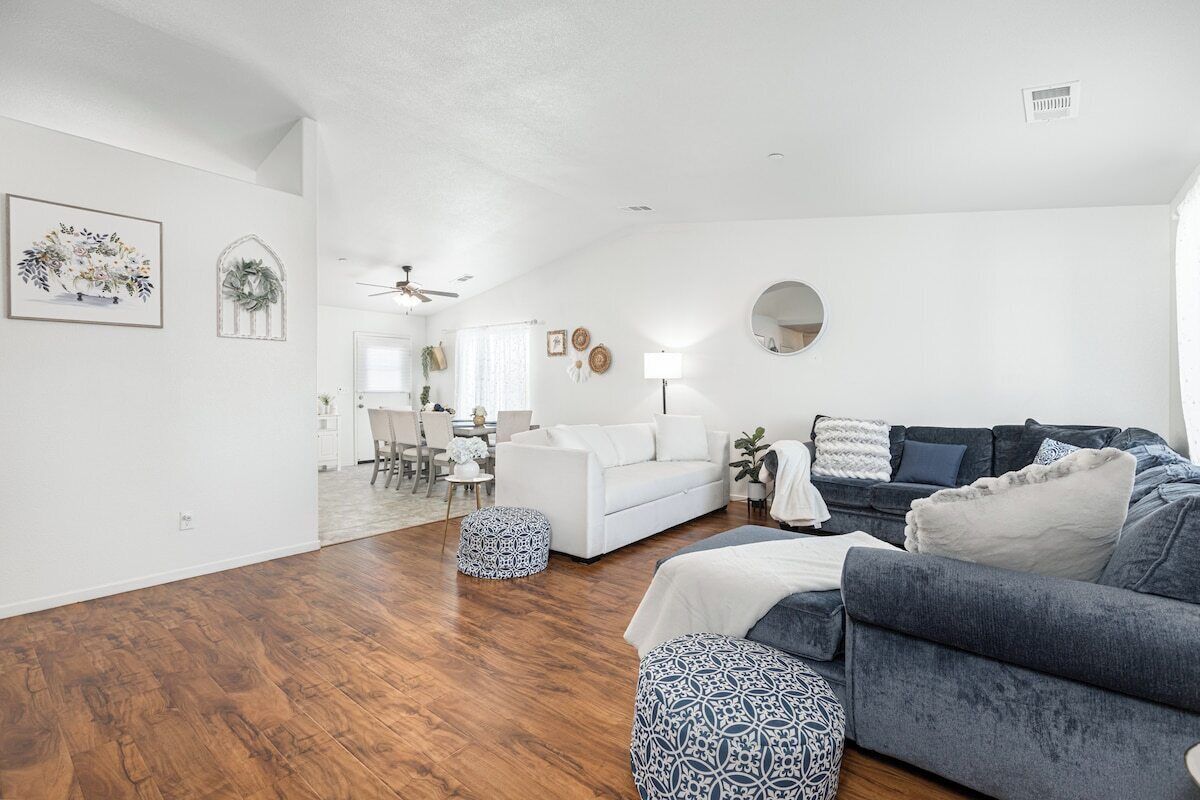 Un salon moderne avec un plancher en bois, un canapé blanc, un canapé bleu et des poufs à motifs.