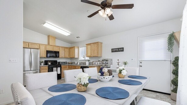 A modern kitchen with wooden cabinets, a coffee bar sign, and a dining area with blue placemats and white chairs. - Bright & Comfy House Near NAS with Free Parking (Armona)