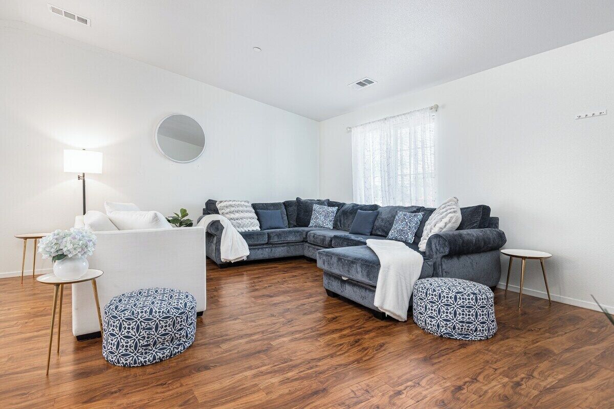 Un salon moderne avec un canapé d’angle, des poufs, un miroir rond et une petite table d’appoint.