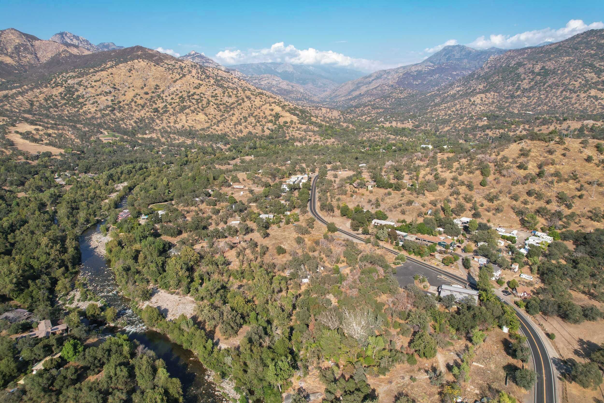 A mountainous landscape with a winding road, scattered buildings, and dense forest areas.