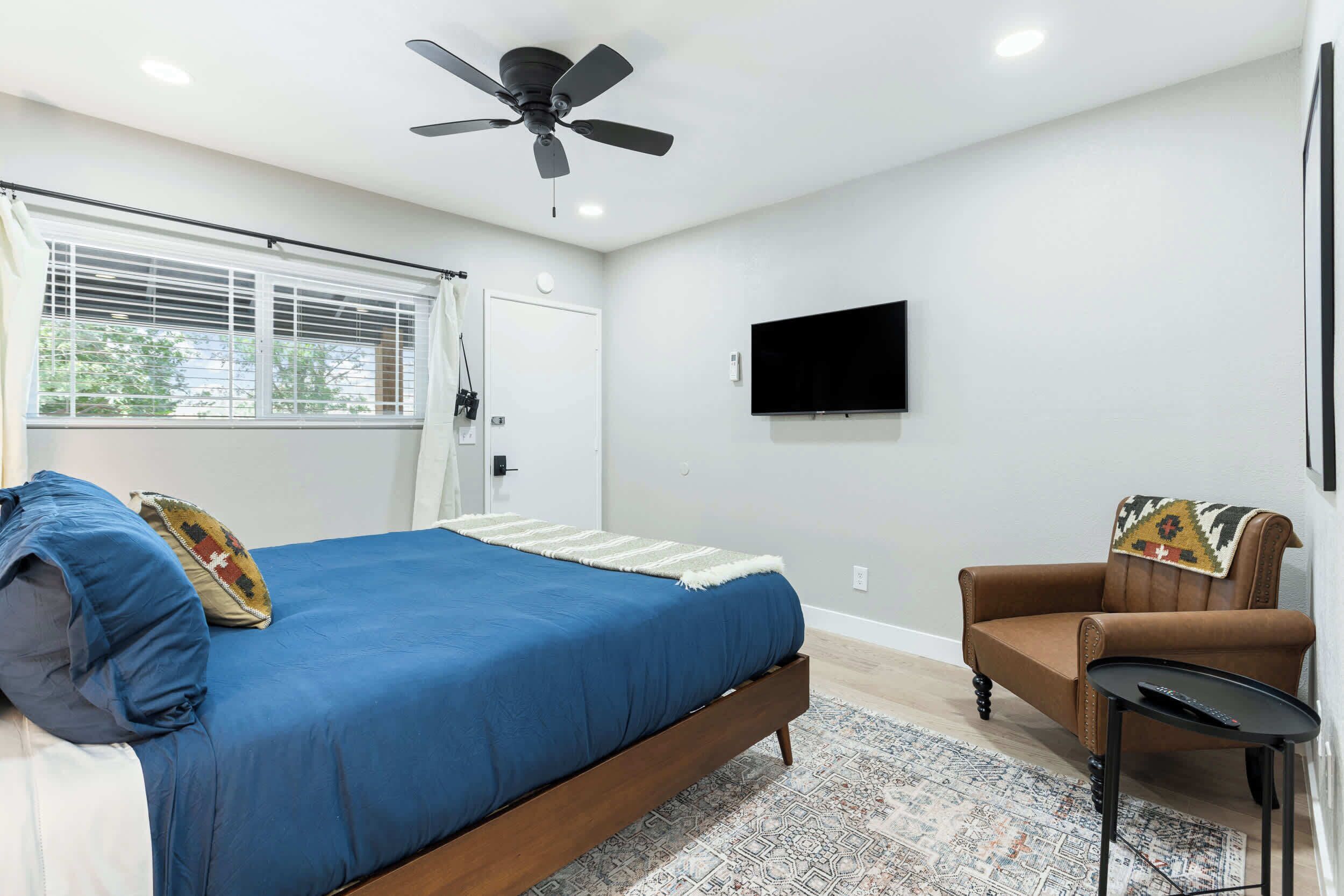 A bedroom with a bed, a chair, a TV, and a ceiling fan.